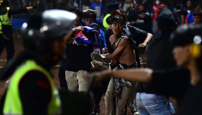 Tumatakbo ang mga kabataang lalaki habang nagpapaputok ng tear gas ang pulis na nag-trigger ng stampede sa Indonesian football stadium noong Sabado ng gabi.  — AFP