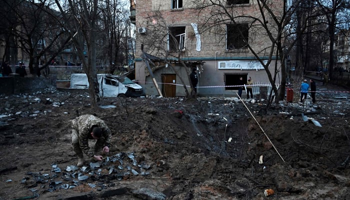 Ang isang serviceman ay nangongolekta ng mga fragment ng missile sa isang bunganga na iniwan ng isang welga ng Russia.  — AFP