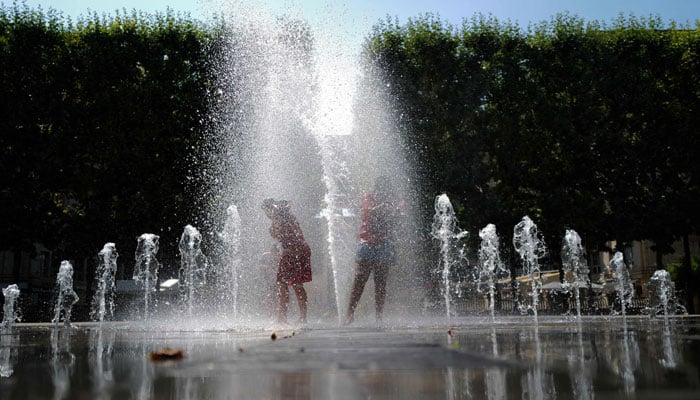 Lumalamig ang mga bata sa ilalim ng water jet sa isang fountain sa panahon ng heatwave sa Montpellier, southern France, noong Hunyo 26, 2023. — AFP